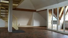 Empty room with wooden staircase, white walls, wooden beams, and red hexagonal tiles on the floor.