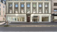 3 story building, multiple windows, glass doors, brown door, concrete sidewalk
