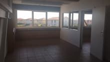 Large open space with tile flooring, multiple windows providing natural light, and a balcony or terrace visible through the windows.