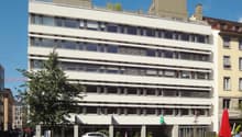 modern office building, white exterior, large windows, ground floor commercial space, surrounding greenery