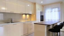 modern kitchen with white cabinets, wooden countertop, stainless steel sink, faucet, black bar stools, white appliances