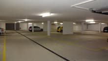 Empty parking area, underground, with yellow markings on the floor and white pillars, 4 cars parked