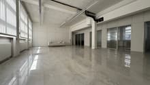 Large open office space with high ceilings, gray marble-like flooring, and a couch in the corner. The space appears to be empty and ready for use.