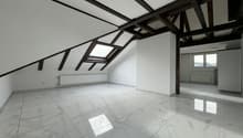 an attic room with a white tiled floor, dark wooden beams on the ceiling, skylights, a white pillar and a heater