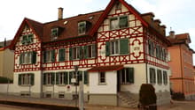 A traditional German half-timbered building with a red tiled roof, green shutters, and decorative wooden beams. The building appears to be a residential or commercial structure, with a sign indicating the year 1898.