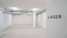 Empty underground garage space, white walls, ceiling pipes, two entrance doors.