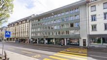 Five story building with green facade, multiple shops on the ground floor, tramway overhead.