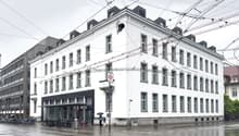 A multi-story white building with ornate architectural details, including windows and a prominent roofline. The building appears to be located in an urban area, with power lines and other infrastructure visible overhead. There are bicycles parked outside