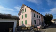 2-story pink house with green shutters, garage, and a stone wall in the front