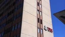 A multi-story commercial building with a prominent UBS logo on the facade. The building has a modern, angular design with large windows and a beige exterior. There is also a BCN logo visible on the building.