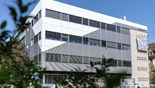 A multi-story office or commercial building with a modern, minimalist design. The building has a white exterior with large windows and a prominent entrance.