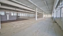 Empty building with high ceiling, large windows, concrete floor, metal beams, and pipes