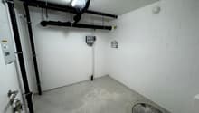 Empty room with concrete floor, white brick walls, pipes, and a drain cover