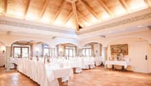 Large dining room with high wooden ceiling, ornate molding, arched windows, white tablecloths, and a fireplace