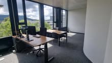 Spacious office with large windows offering a scenic view of the surrounding landscape, including hills and greenery. The office is equipped with desks, chairs, and computer equipment, providing a functional workspace.