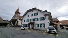white house, green shutters, brown roof, parking lot, 2 cars parked