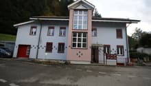 Two-story building, white and pink facade, multiple windows, red entrance door, brown roof, located on a road
