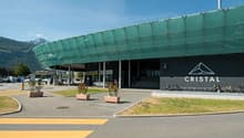 modern architecture with green panels, bike stands, front entrance with stairs, and a parking lot with cars
