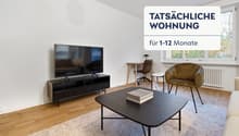 Spacious living room with hardwood floors, large windows, TV stand, coffee table, and a comfortable armchair. The room has a modern and minimalist design.