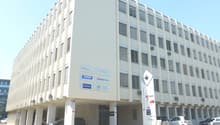 Large office building, white walls, multiple floors, glass windows, underground parking, multiple cars parked.