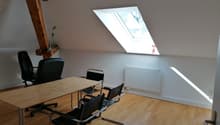 Attic office space with wooden beams, large skylight window, wooden desk, black office chairs, and hardwood flooring.