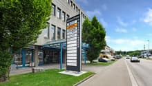 office building with glass walls, 2 story, large trees in front, car parked on street, sign board