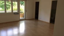 Spacious living room with hardwood floors, large windows overlooking a balcony or terrace, and neutral-colored walls.