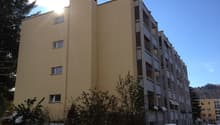 Multi-story building, yellow exterior, multiple windows, balconies, snow on the ground, car parked in front