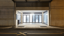 Empty entrance with double doors, tiled floor, large windows, concrete walls, small stone planter