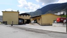 Large yellow building with multiple garages, vehicles parked in front, mountains in the background