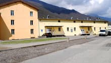 Yellow building, multiple windows, cars parked in front, mountains in the background