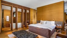 Master bedroom with wooden walls, large bed, bathtub, wooden chair, wooden table, wooden floor, white ceiling