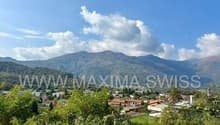 A panoramic view of a town with buildings, mountains, and a river.