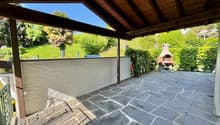 Terrace with wooden roof, fireplace, paved floor, wall, greenery, garden.