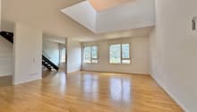 Spacious living room with hardwood floors, white walls, and a skylight providing natural light. The room has a clean, open layout.