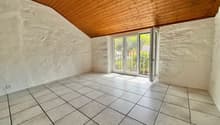 A room with white tiled floor and white walls, a glass door, wooden ceiling and an electric outlet on the wall.