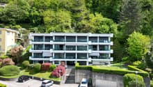 3 story apartment building, white exterior, large windows, balconies, parking area, green surroundings