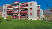 Multi-story building, grey exterior, red balconies, green front lawn, mountain backdrop