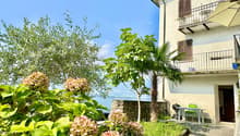 Two-story house with balcony, stone wall, garden, and lake view