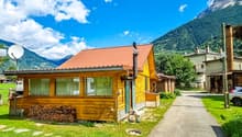 wooden house, metal roof, window shutters, green lawn, mountains in background