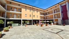 Modern multi-story building with a paved courtyard, balconies, multiple entrances, and trees.
