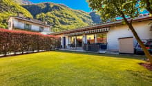 Two houses, with white walls, green lawn, mountain in the background