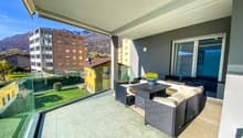 Balcony with glass railings, wooden furniture, potted plant, tiled floor, green lawn view