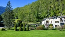 large house with garden, well-maintained green lawn, surrounded by trees, mountains in the background