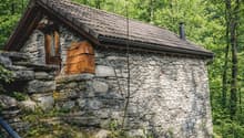 Stone house, brown roof, wooden door, surrounded by trees
