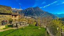 Stone house, stone bench, clothesline, green grass, mountain view