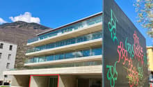 Modern building with glass windows, concrete structure, graffiti on the wall, green lawn, mountains in the background