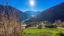 Green grass, two houses, mountains, lake, clear sky, sun