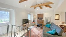 living room with wooden beams, gray couch, blue pillows, wooden desk, TV, wooden cabinet, mirror, radiator, window with view