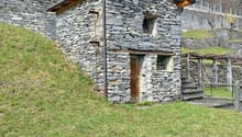 Stone house, wooden roof, wooden door, two windows, located on a slope